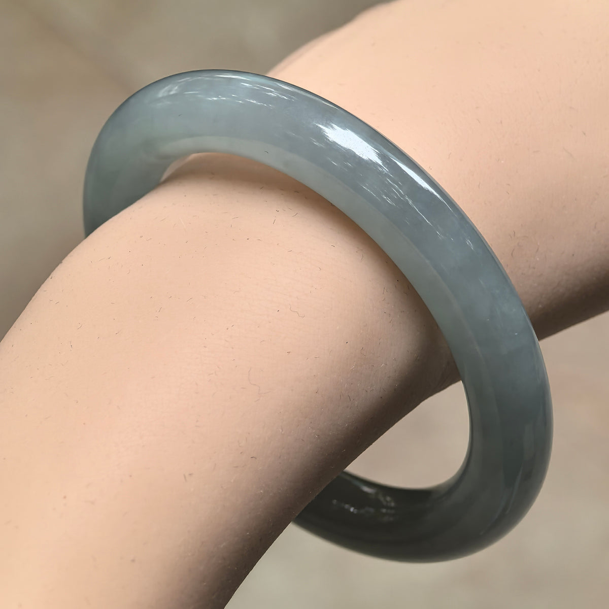 Angled wrist view of a blue-green jadeite round-bar bangle, showing its smooth curves and softly translucent appearance.