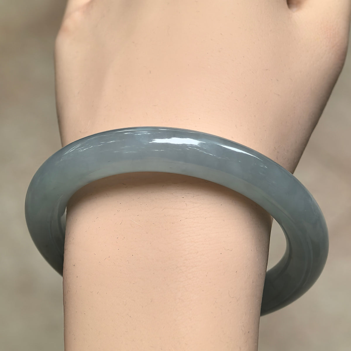 Front wrist view of a blue-green icy glutinous jadeite round-bar bangle, showing its full rounded profile and polished luster.