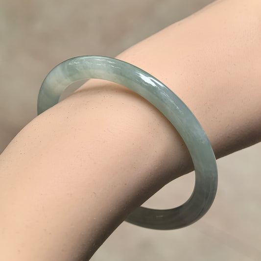 Angled wrist view of a slim pale green jadeite round-bar bangle, showing its translucent appearance and delicate proportions.