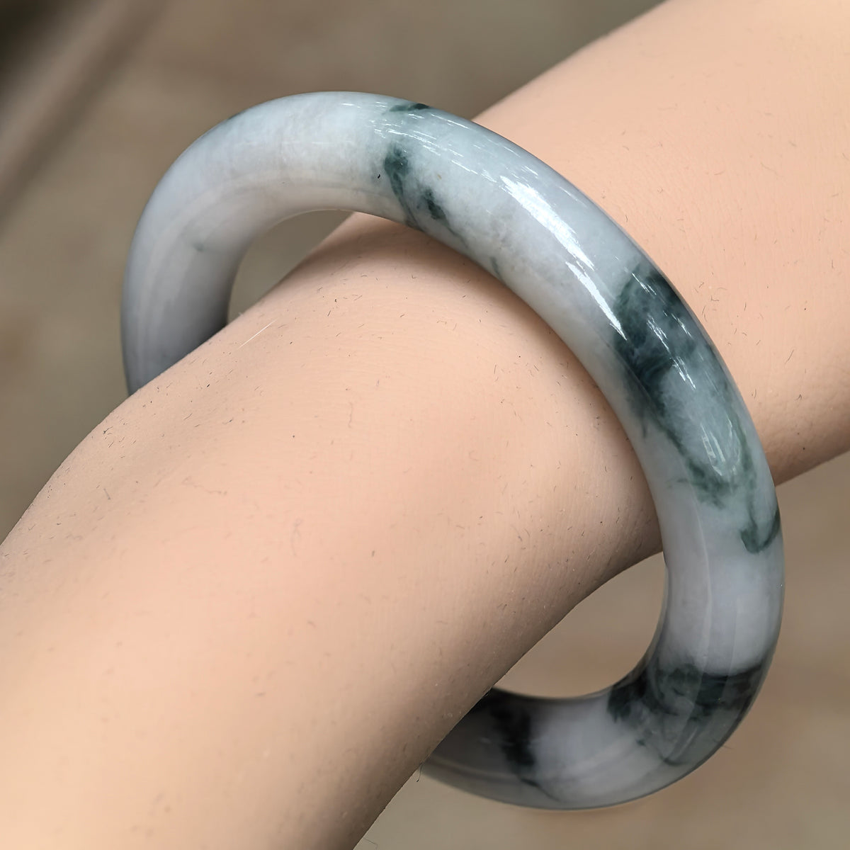 Angled wrist view of a milky white round-bar jadeite bangle with flowing dark green patches.