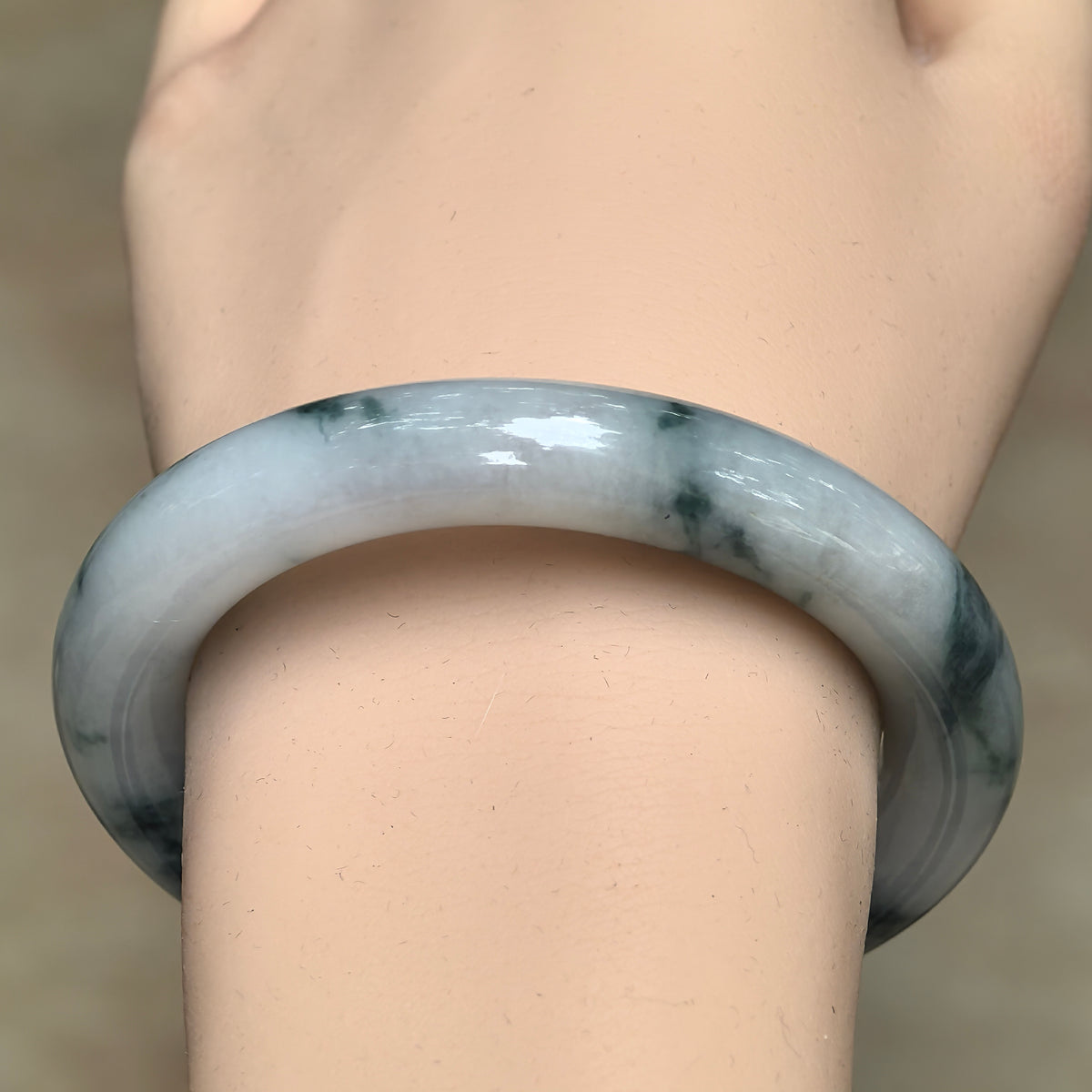Front wrist view showing the rounded profile and dark green wisps of a milky white jadeite bangle.