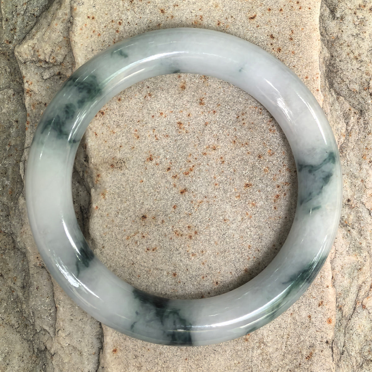 Top view of a round-bar jadeite bangle on stone, with dark green markings contrasting against its milky white base.