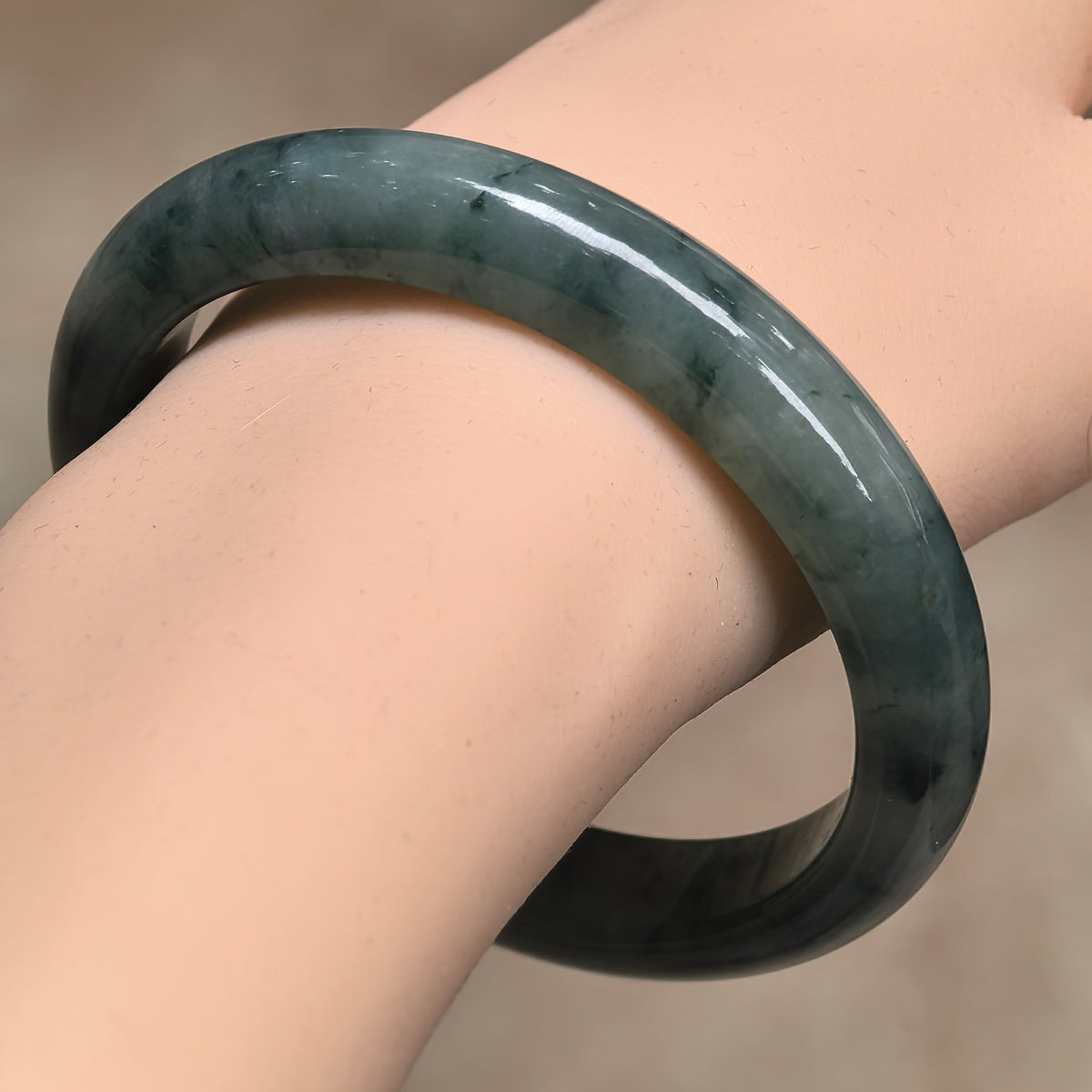 Angled wrist view of a deep green D-shape jadeite bangle with darker floating patterns and a polished outer surface.