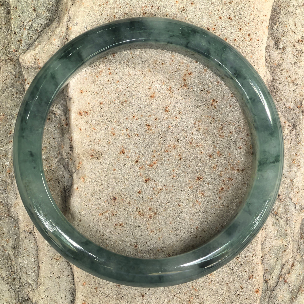 Top view of a deep green jadeite bangle on stone, with fine branching wisps and darker patches distributed around the band.