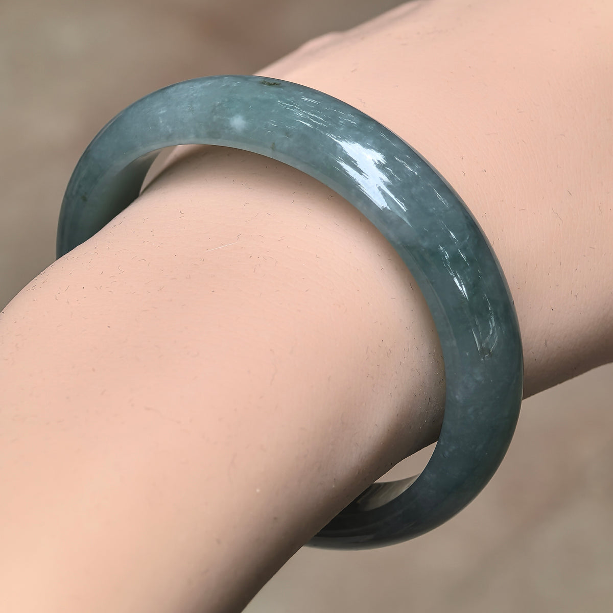 Angled wrist view of a blue-green oval jadeite bangle, showing its broad polished face and softly clouded texture.