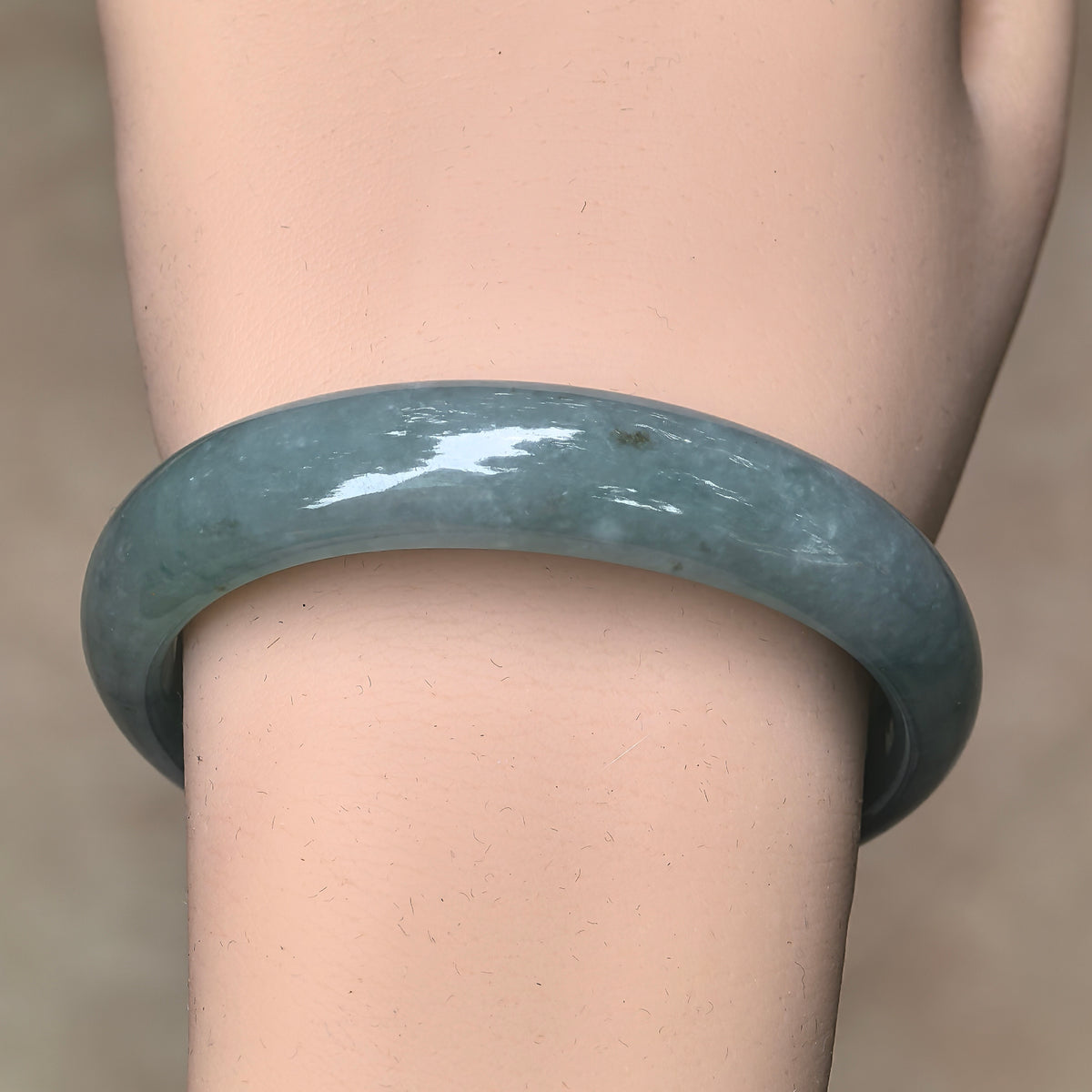 Front wrist view of a glutinous blue-green jadeite bangle with small surface pits visible along the outer face.