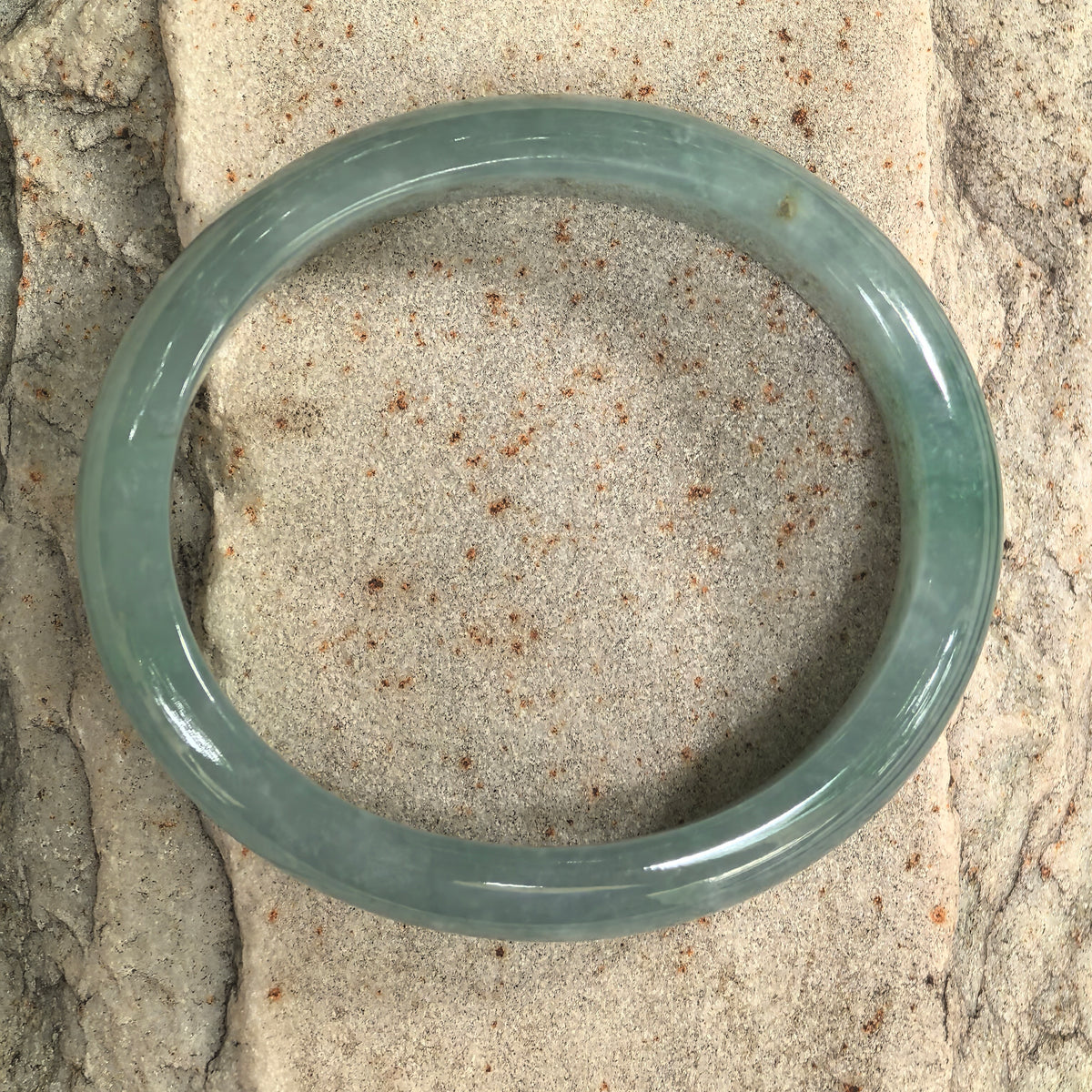 Top view of a blue-green jadeite bangle on stone, showing its oval opening, polished edges, and small surface pits.