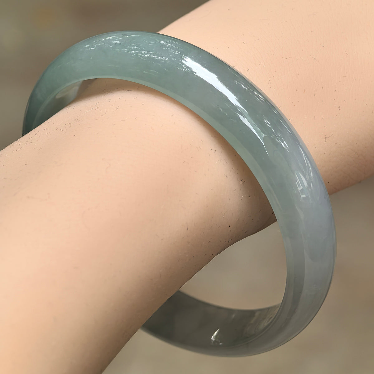 Angled wrist view of a pale green icy glutinous jadeite bangle, showing its broad rounded outer face and polished luster.