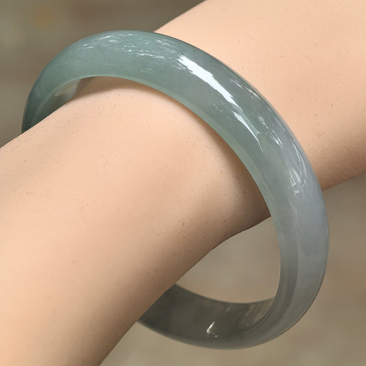 Angled wrist view of a pale green icy glutinous jadeite bangle, showing its broad rounded outer face and polished luster.