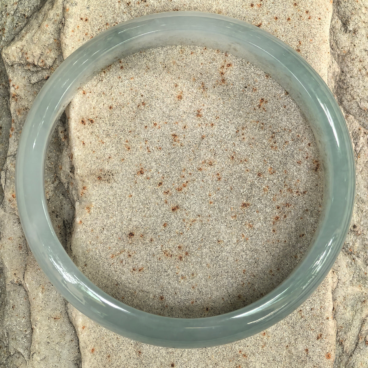 Top view of a pale green D-shape jadeite bangle on stone, showing its circular outline and softly translucent band.