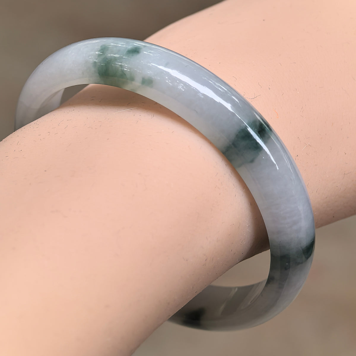 Angled wrist view of a fine glutinous jadeite D-shape bangle, showing green patches against a milky white base.