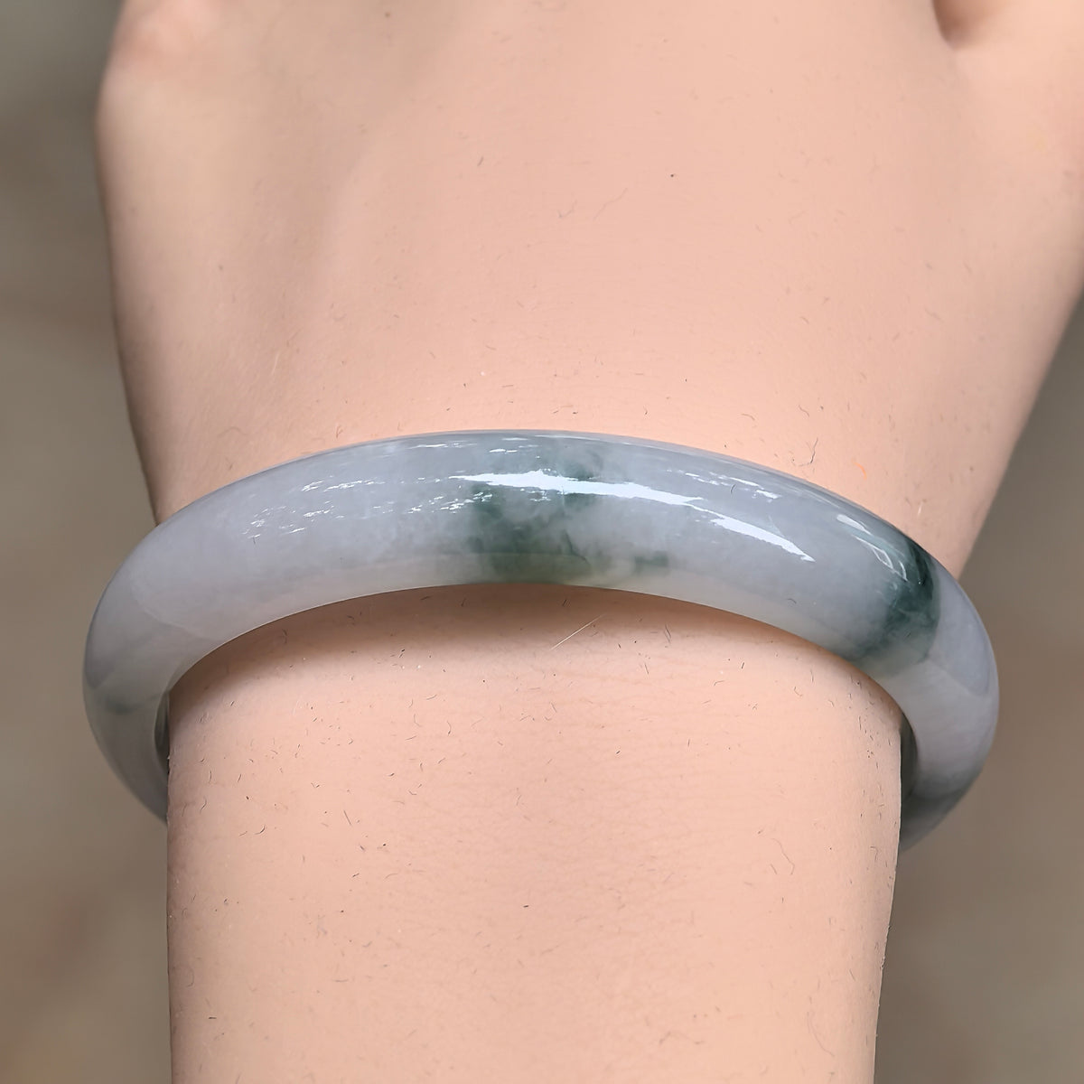 Front wrist view of a white and green jadeite bangle with clustered floating patterns and a polished rounded outer surface.