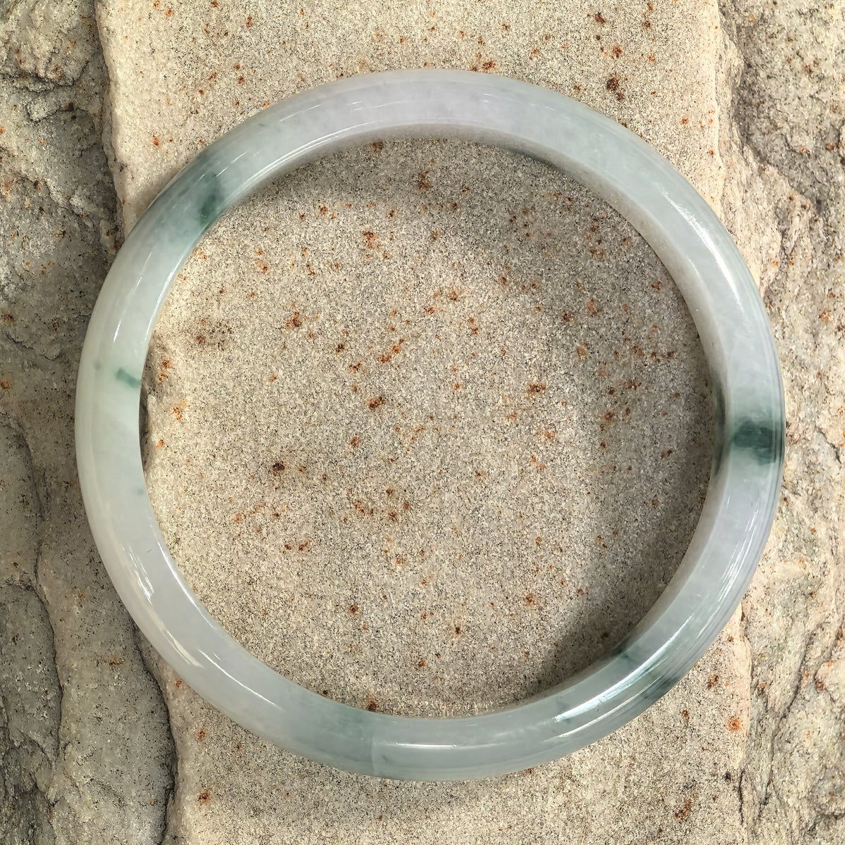 Top view of a D-shape jadeite bangle on stone, with green floating patterns spaced around a milky white band.