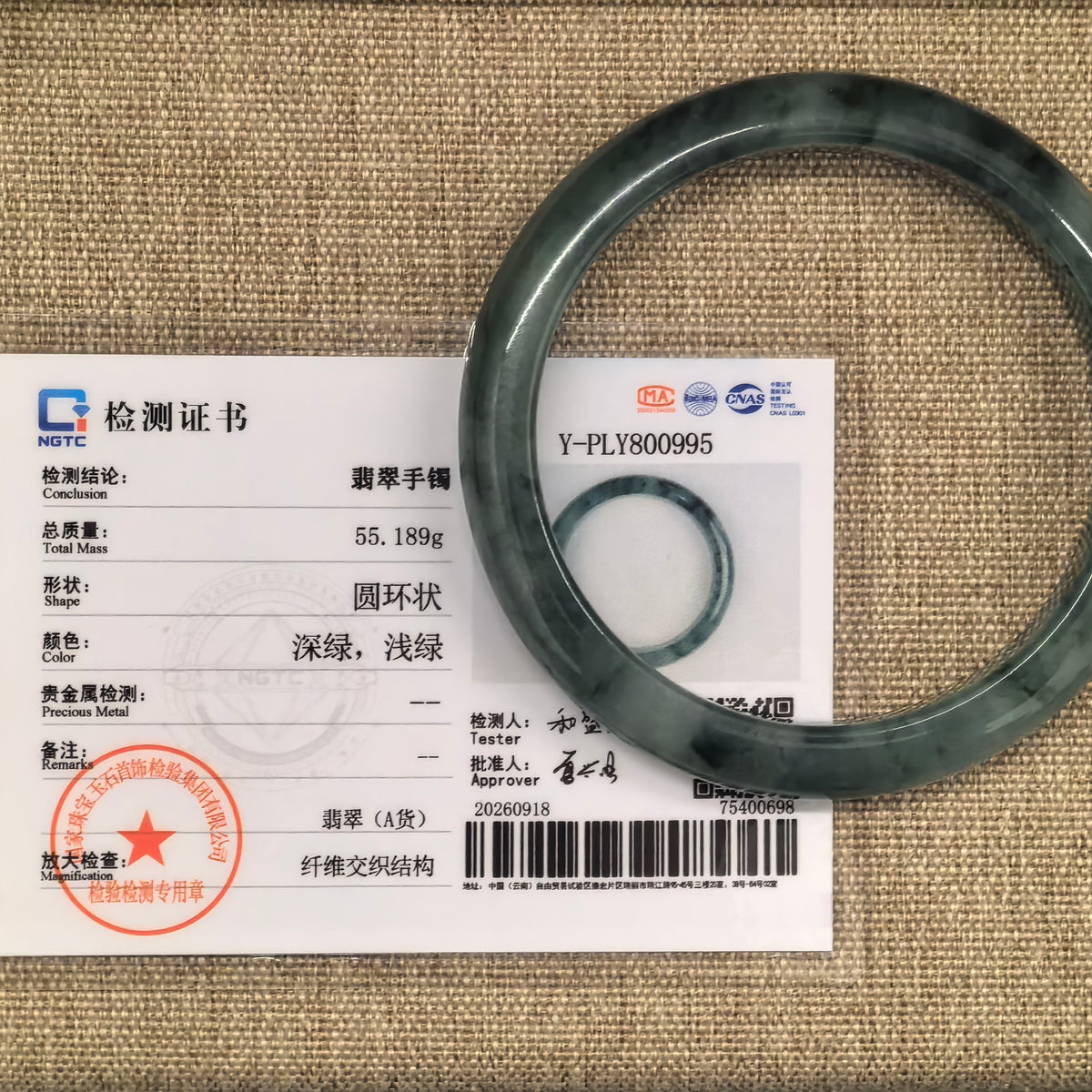 Deep green jadeite bangle displayed with its matching NGTC certificate on a woven background.