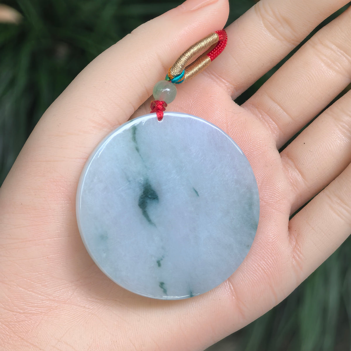 Large white and green jadeite round plain plaque pendant resting in an open palm, showing its proportions and decorative cord.