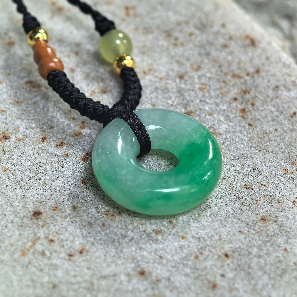 Angled view of a fine glutinous jadeite donut pendant on pale stone, showing its rounded profile and concentrated green accents.