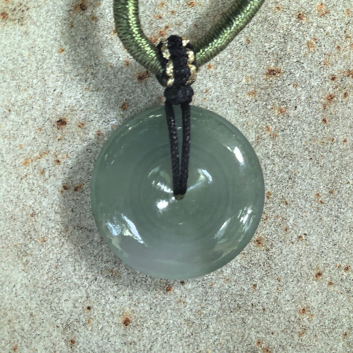 Top view of an icy glutinous gray-green jadeite peace pendant on stone, with a small central opening and reflective polished surface.