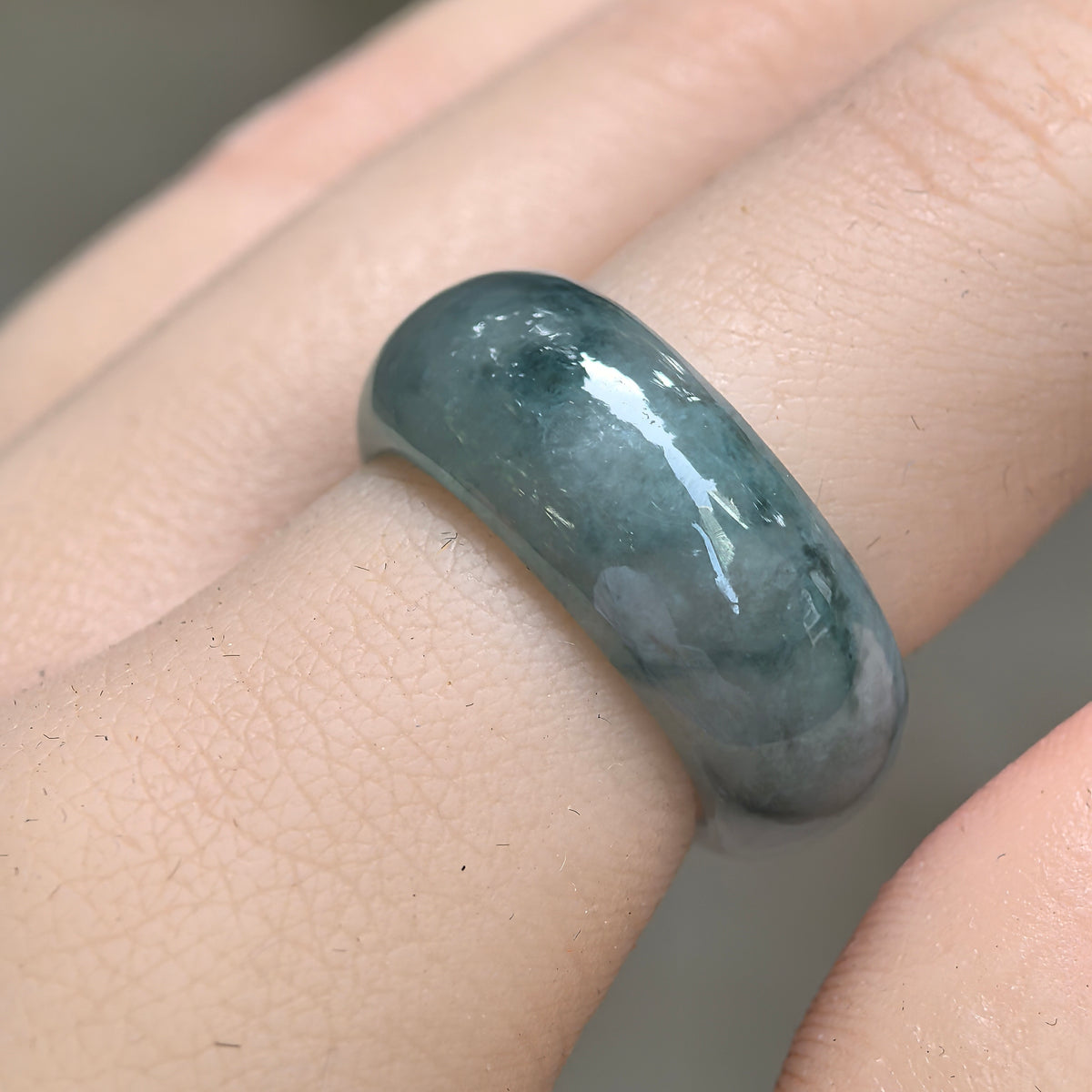 Angled close-up of a wide jadeite ring band worn on a finger, showing deep green floating patterns and a polished rounded surface.