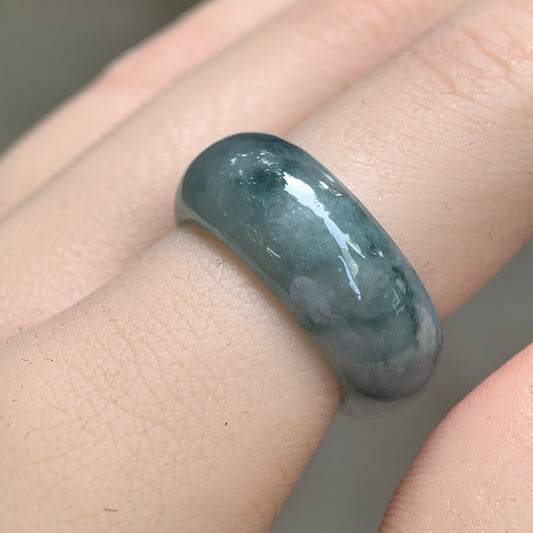 Angled close-up of a wide jadeite ring band worn on a finger, showing deep green floating patterns and a polished rounded surface.