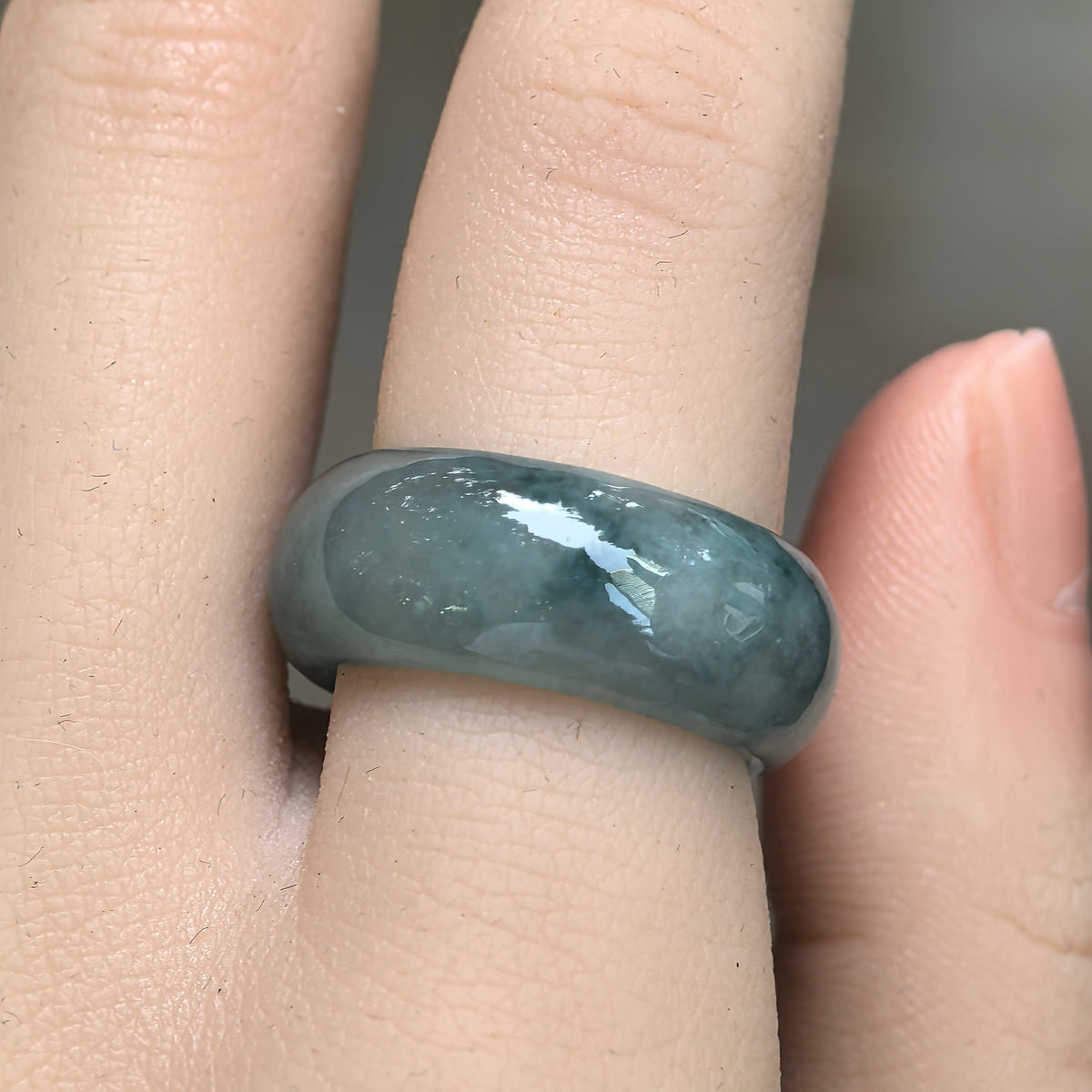 Front view of a green jadeite ring band on a finger, highlighting its broad profile and softly clouded icy glutinous texture.