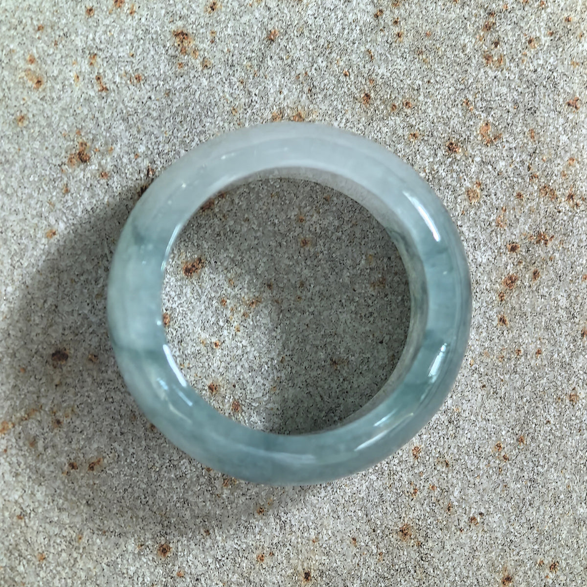 Top view of a jadeite ring band resting on stone, showing its circular opening and green patterns around the pale green band.