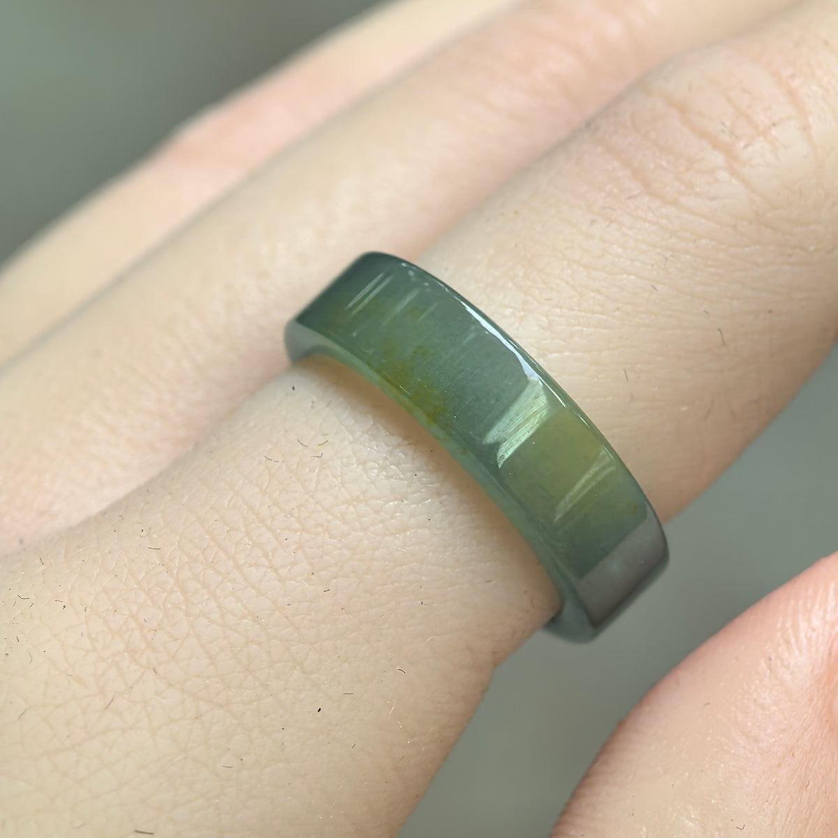 Angled view of a straight-cut jadeite ring band on a finger, highlighting the polished green surface and localized yellow coloring.