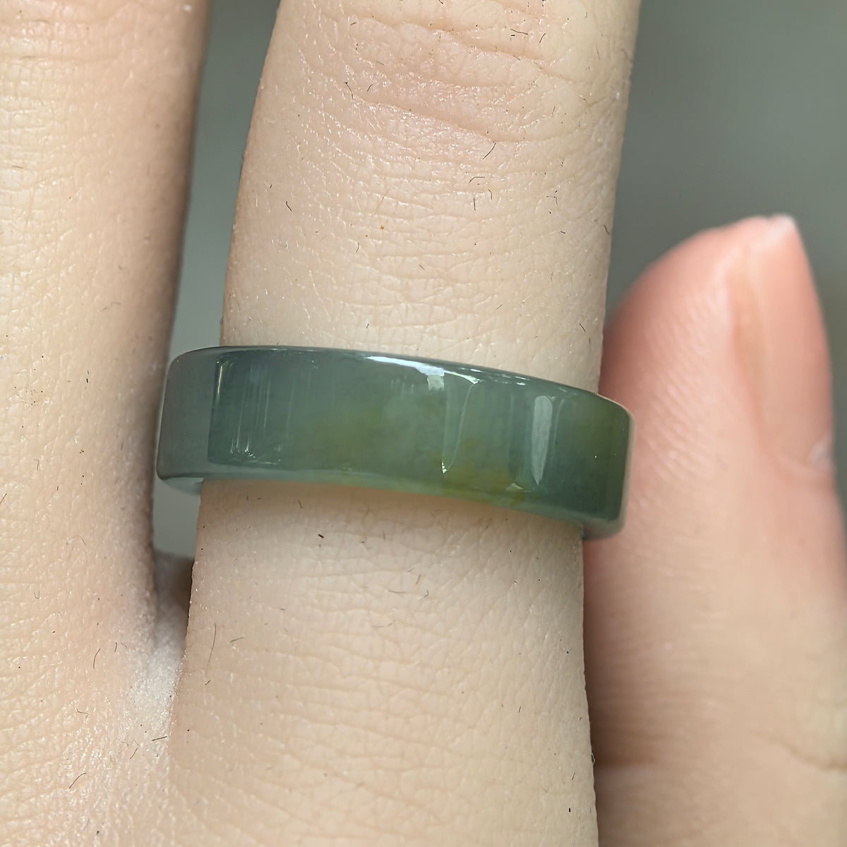 Front view of a green jadeite ring band worn on a finger, showing its flat outer surface and subtle yellow accent.