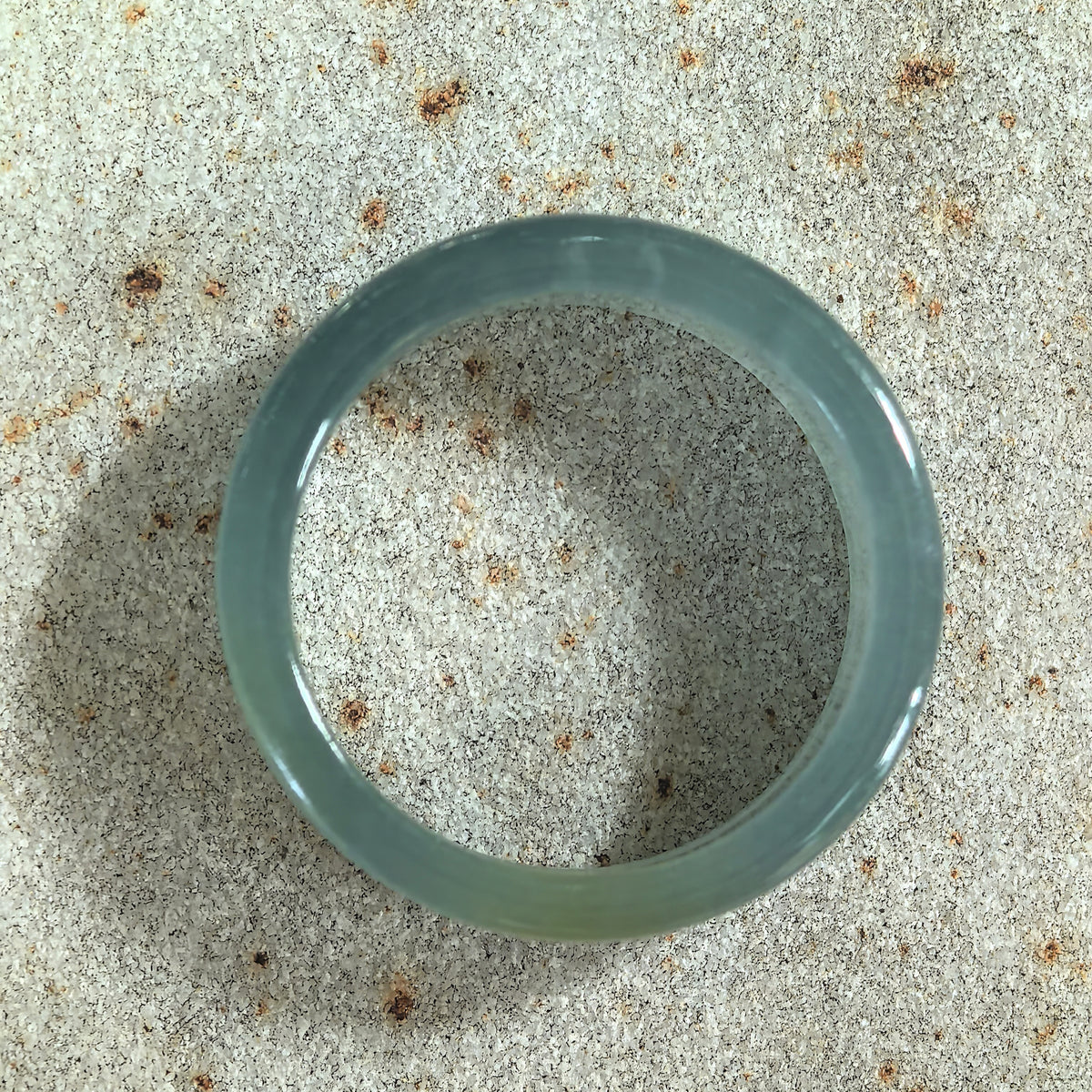 Top view of a green jadeite ring band on stone, showing its circular opening, polished edges, and subtle yellow section.