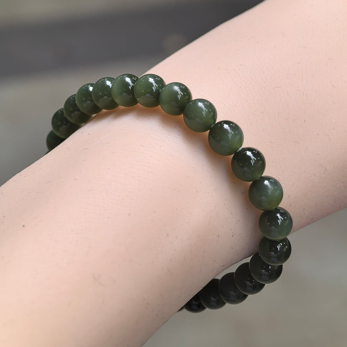 Angled wrist view of a deep green Hetian nephrite bead bracelet, showing polished round beads and soft variations in color.