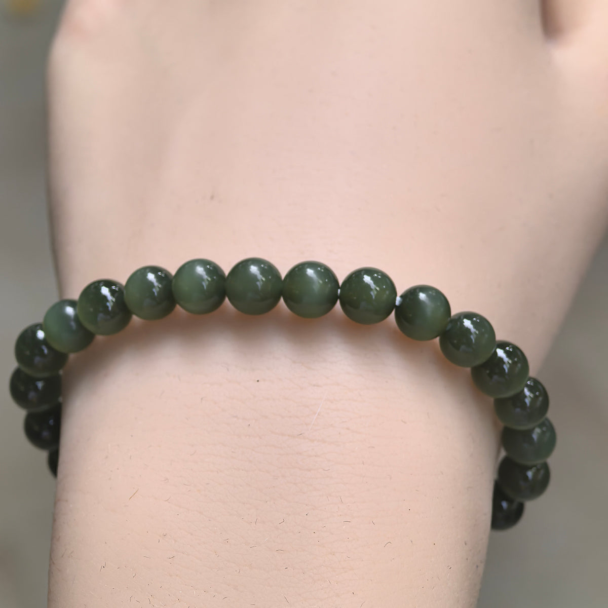 Front wrist view of a dark green nephrite bracelet, highlighting its small round beads and simple single-strand design.