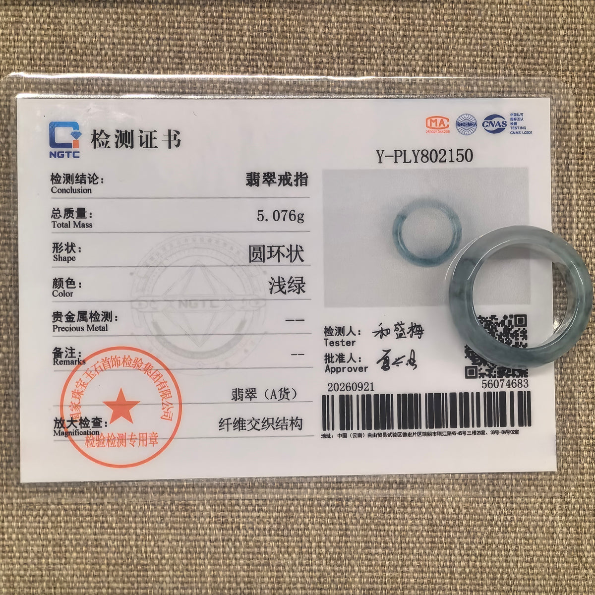 Green jadeite ring band displayed with its matching NGTC certificate on a woven background.