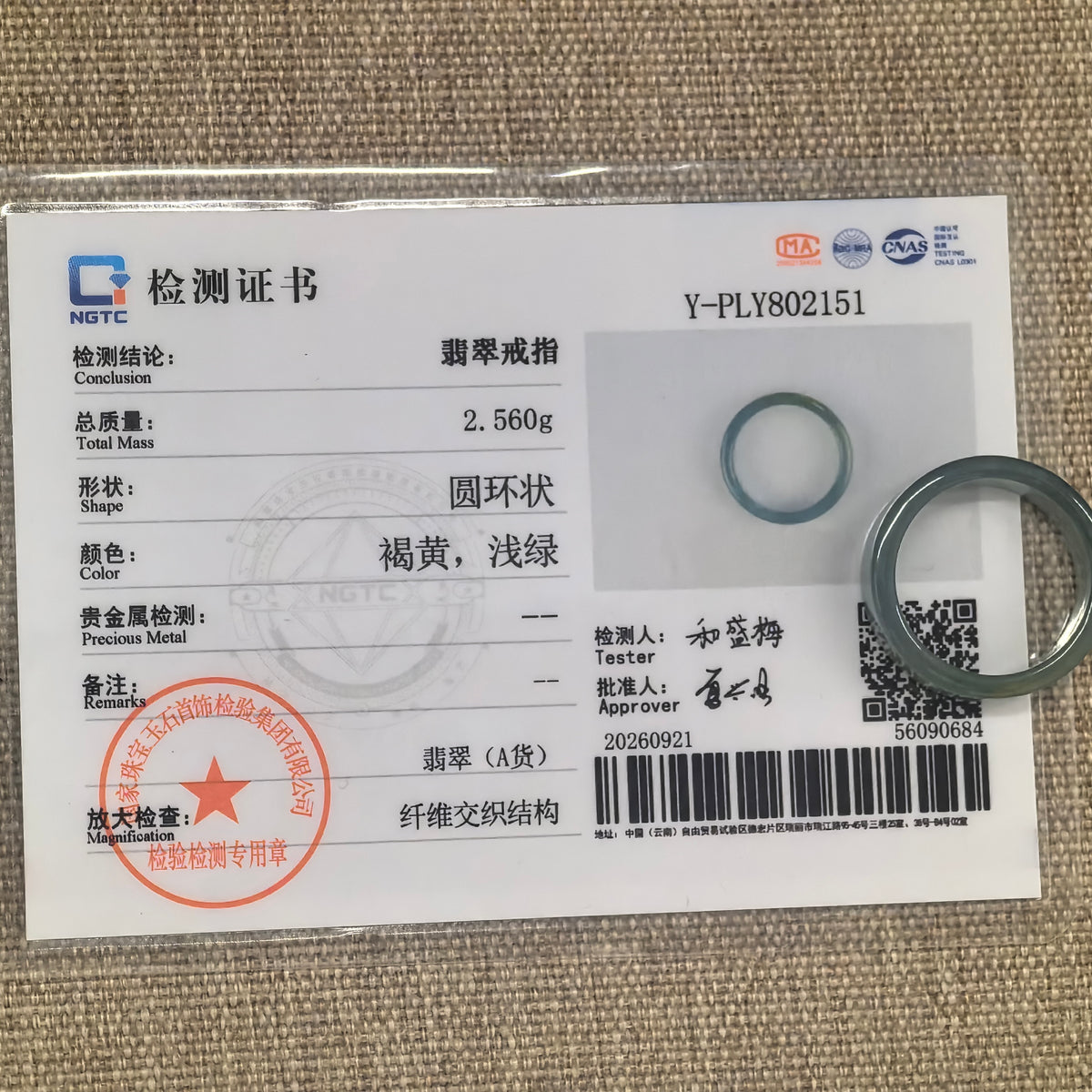 Green jadeite ring band displayed with its matching NGTC certificate on a woven background.