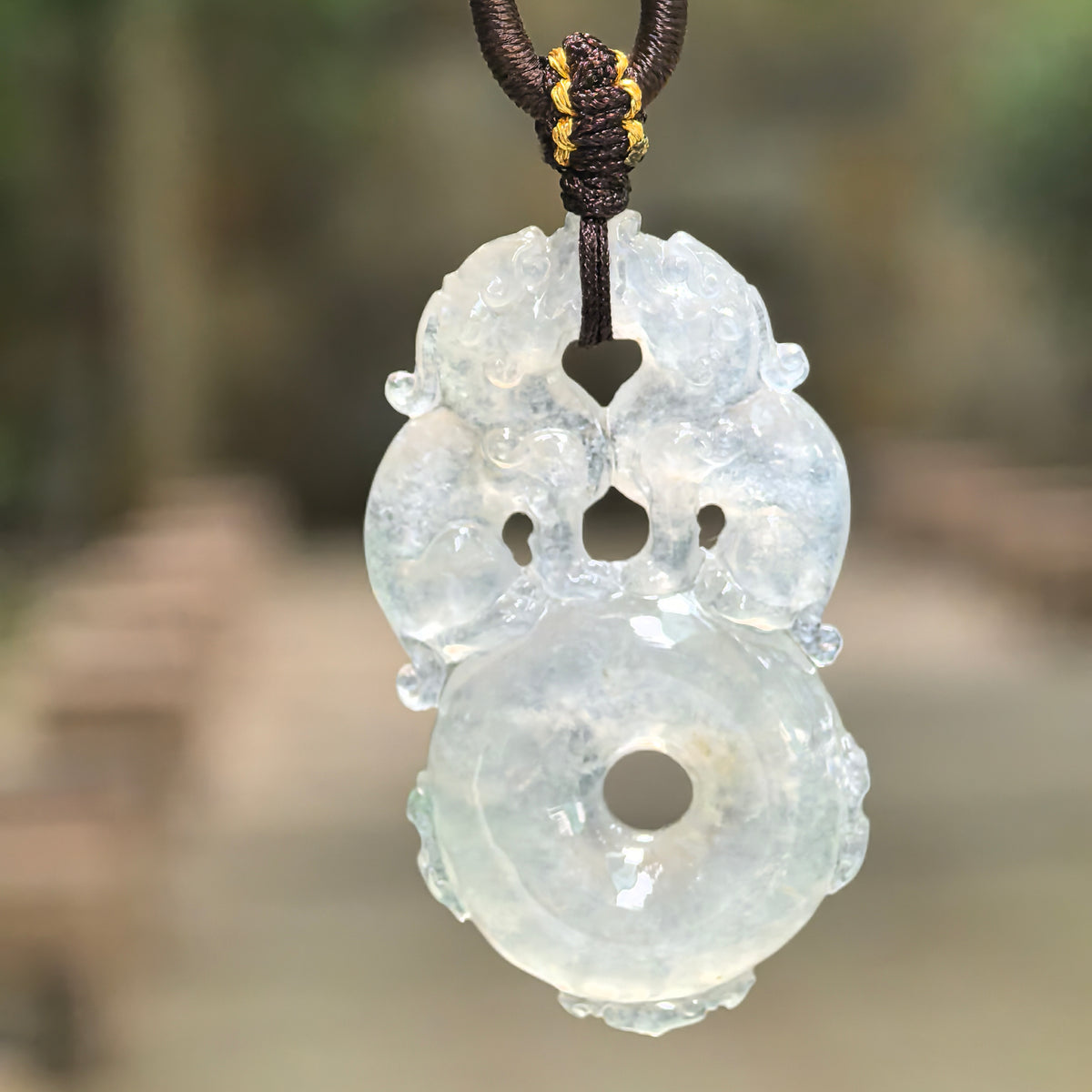 Double Pixiu jadeite peace pendant suspended from a knotted cord, with natural light highlighting its translucency and carved details.