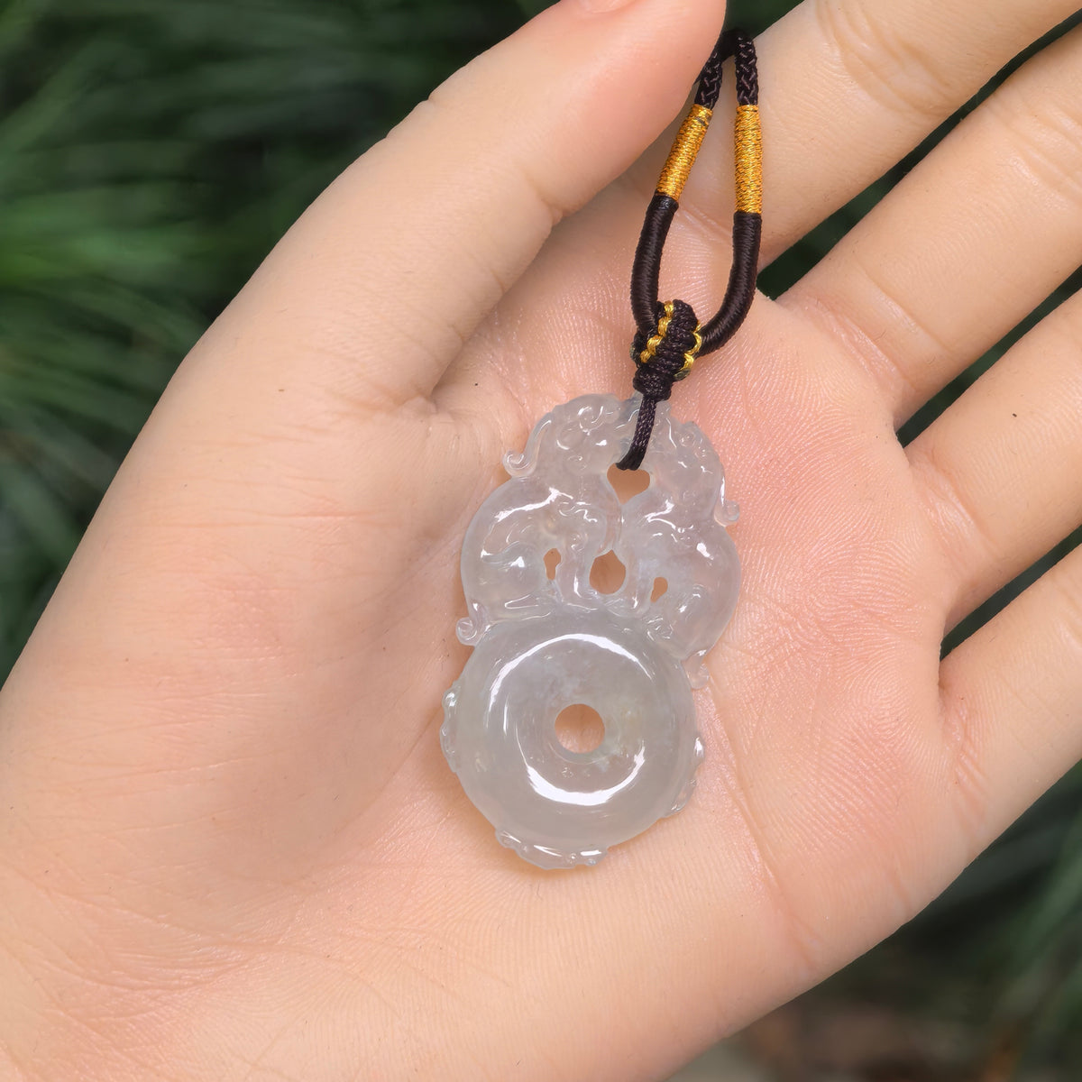Jadeite pendant with a subtle pale green tint resting on an open palm, showing two Pixiu standing on a circular peace pendant motif.