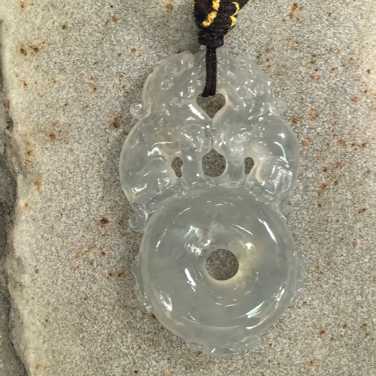 Front view of a pale green jadeite pendant on stone, showing paired Pixiu figures above a circular peace pendant motif with a central opening.