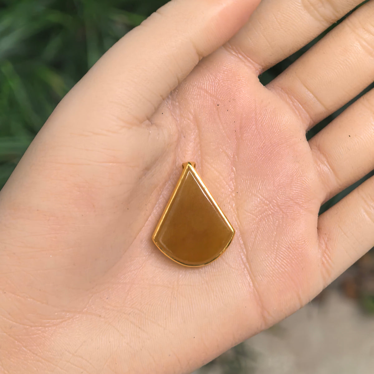 Honey-yellow jadeite teardrop pendant resting on an open palm, showing its proportions, polished face, and narrow 18K gold frame.