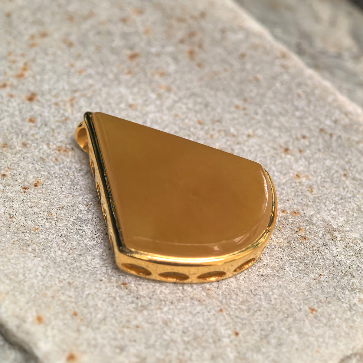 Angled close-up of a yellow jadeite teardrop pendant on stone, showing the 18K gold setting and small openings along its side.