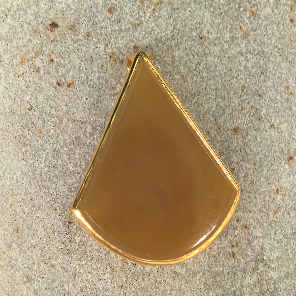 Front view of a yellow jadeite teardrop pendant on a stone surface, highlighting its pointed top, rounded base, and gold border.