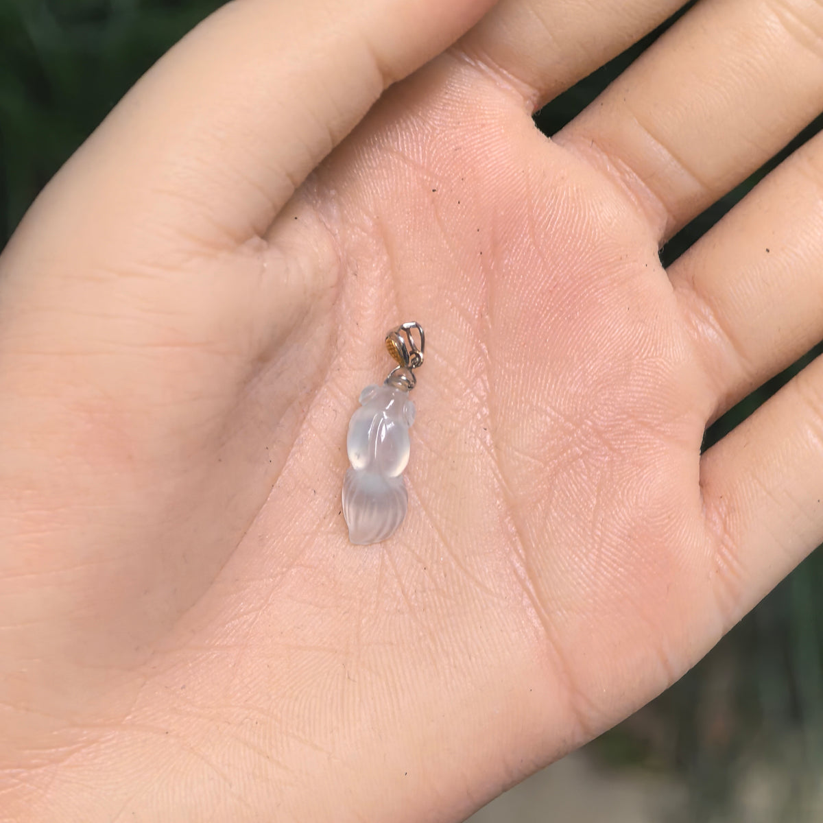 Small white jadeite goldfish pendant resting on a palm, showing its proportions, carved tail, and gold bail.