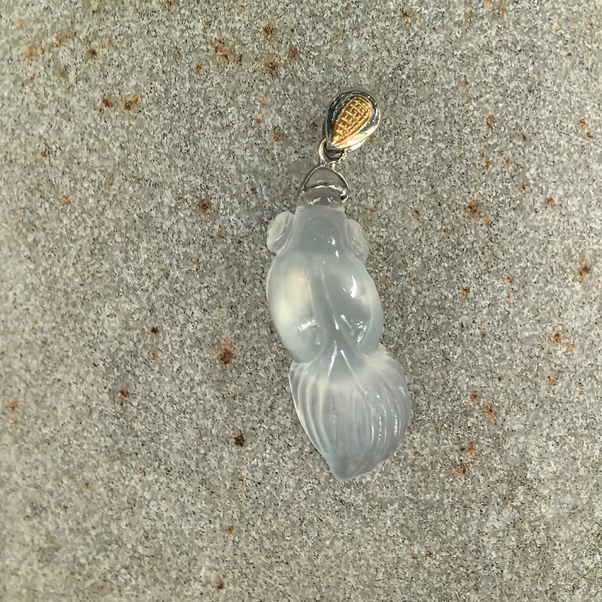 Front view of an icy white jadeite goldfish pendant on stone, showing its prominent eyes, flowing tail, and decorative 18K gold bail.