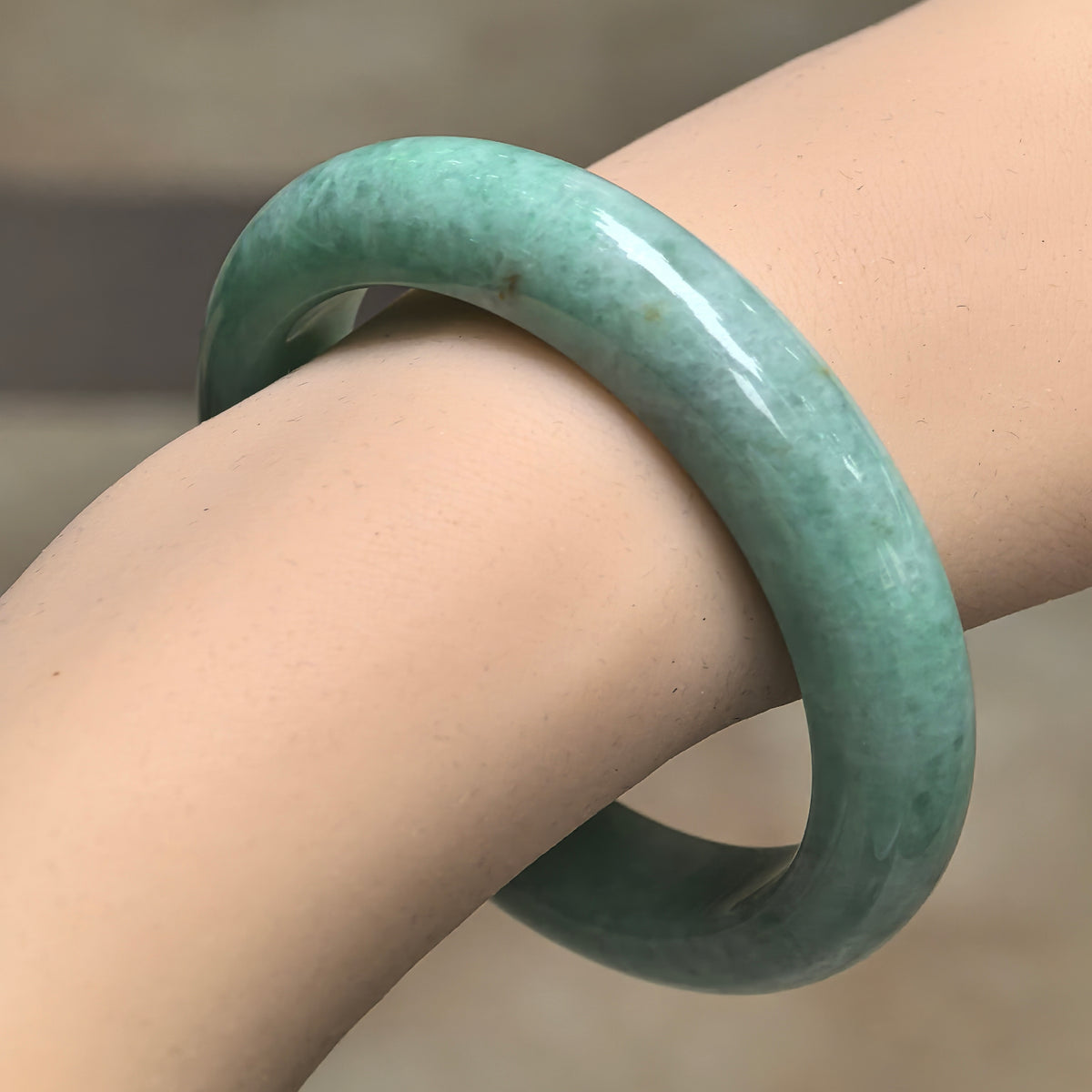 Angled wrist view of an apple green jadeite D-shape bangle, showing its rounded outer surface and softly mottled texture.