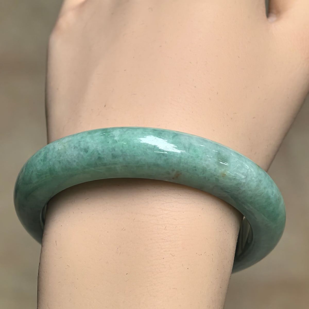 Front wrist view of a glutinous apple green jadeite bangle with visible cotton-like patches beneath its polished surface.