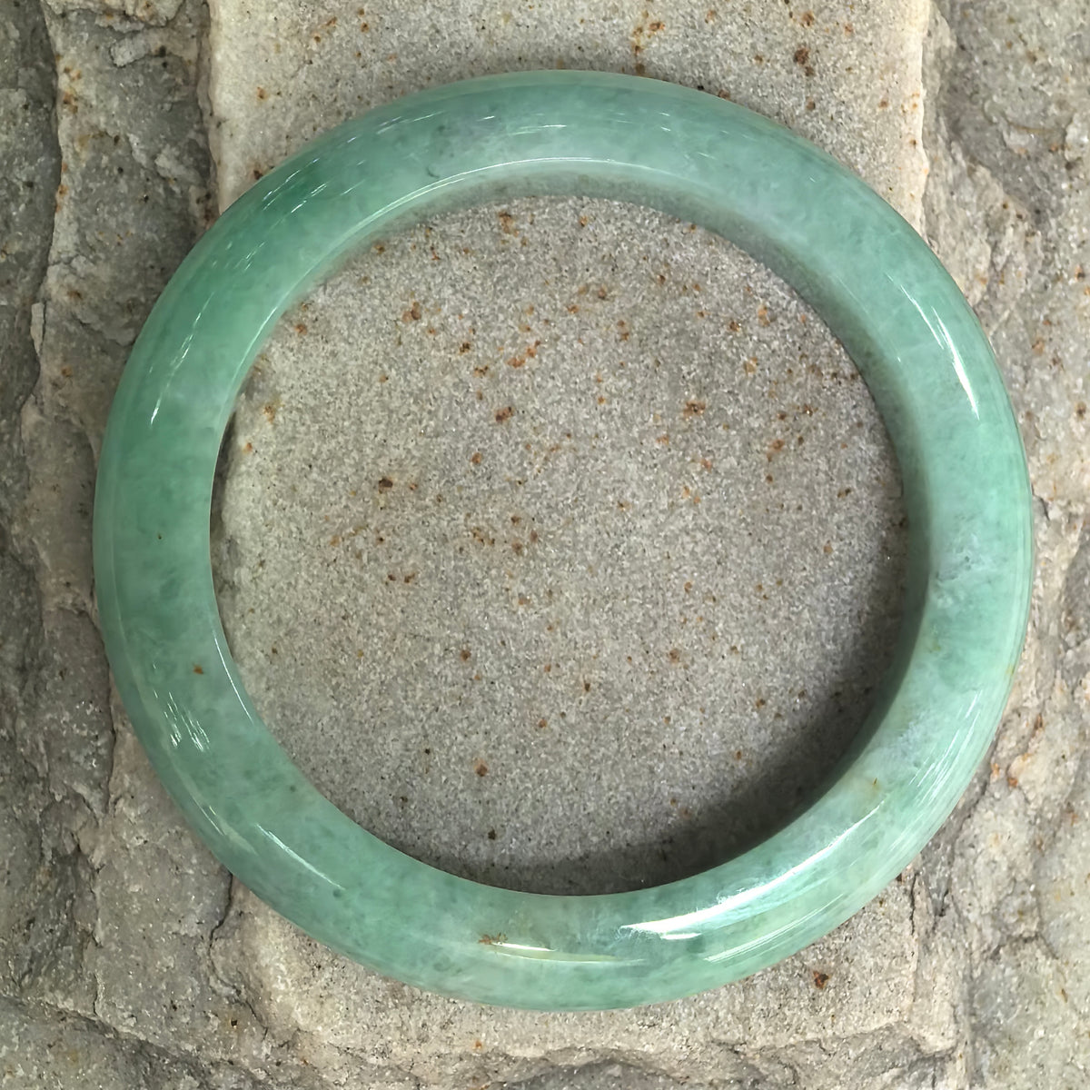 Overhead view of an apple green jadeite bangle on stone, showing green color around the full circle and gentle tonal variations.