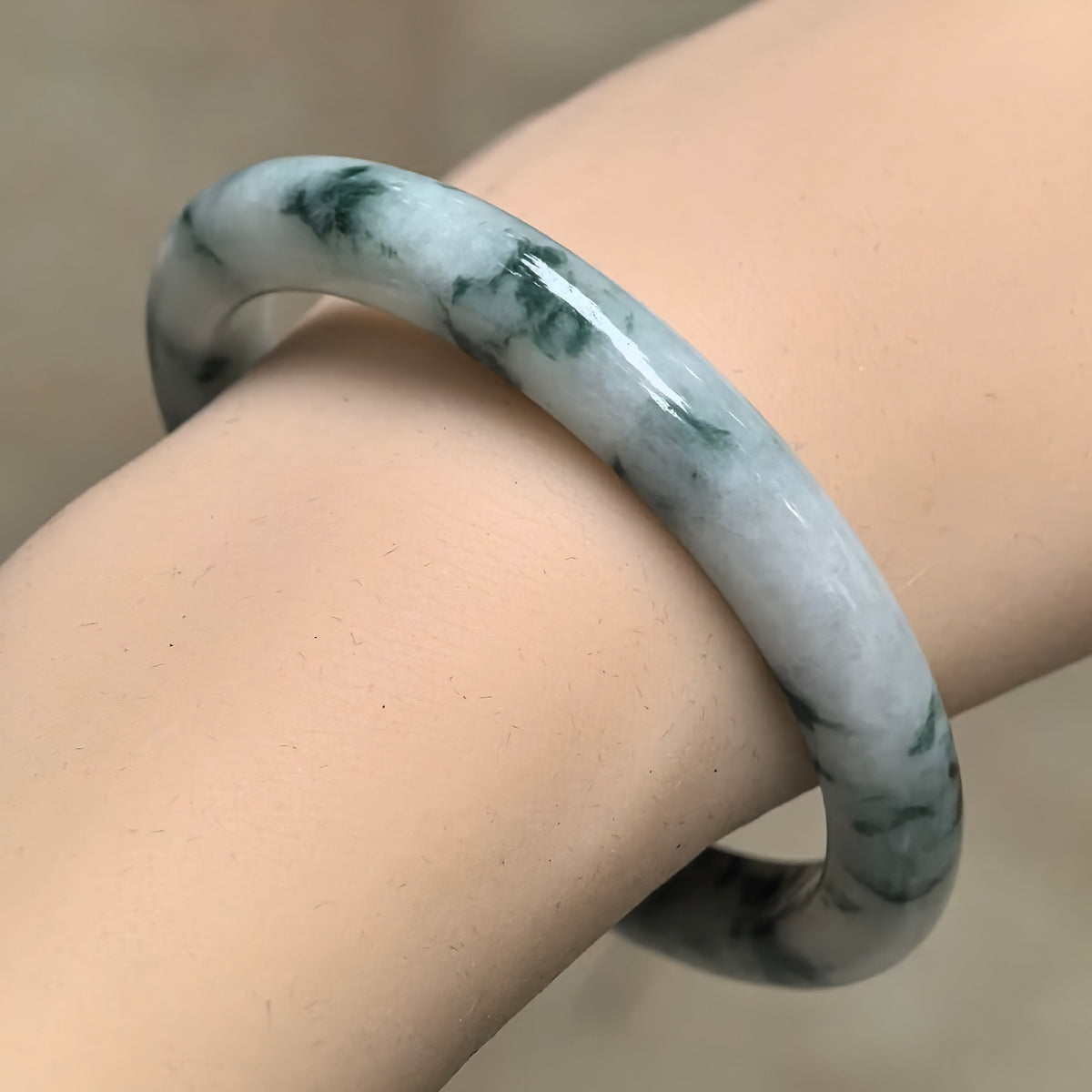 Angled wrist view of a slim jadeite bangle with a milky white base and deep green floating patterns.