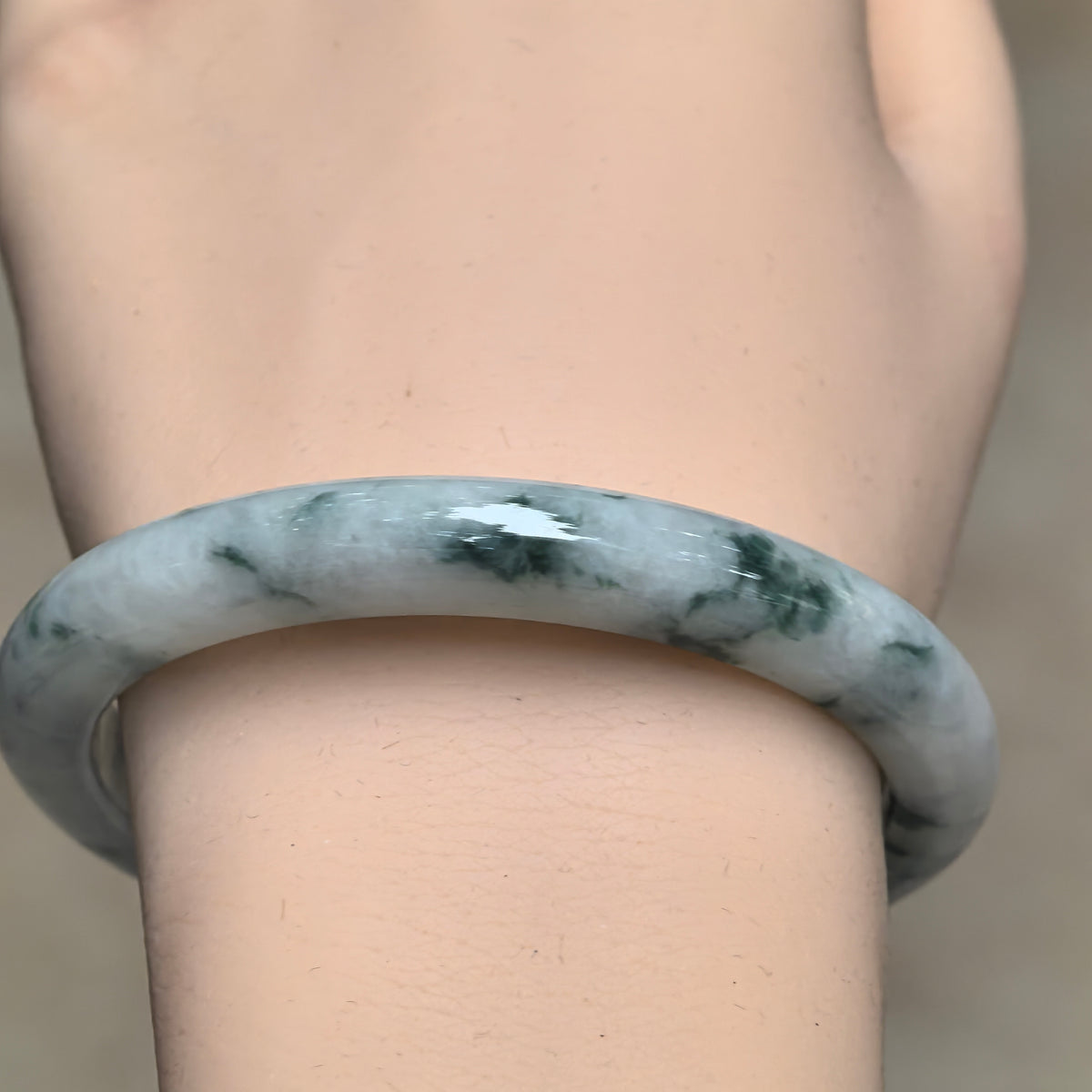 Front wrist view of a white and deep green jadeite bangle, showing its polished surface and branching green patterns.