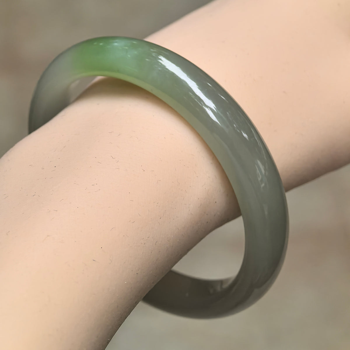 Greenish white Hetian nephrite D-shape bangle worn on the wrist at an angle, showing its vivid green accent and polished outer curve.