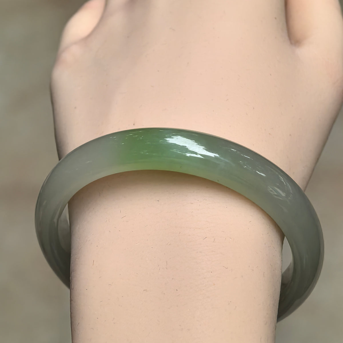Front view of a greenish white Hetian jade bangle on the wrist, highlighting the localized bright green section.