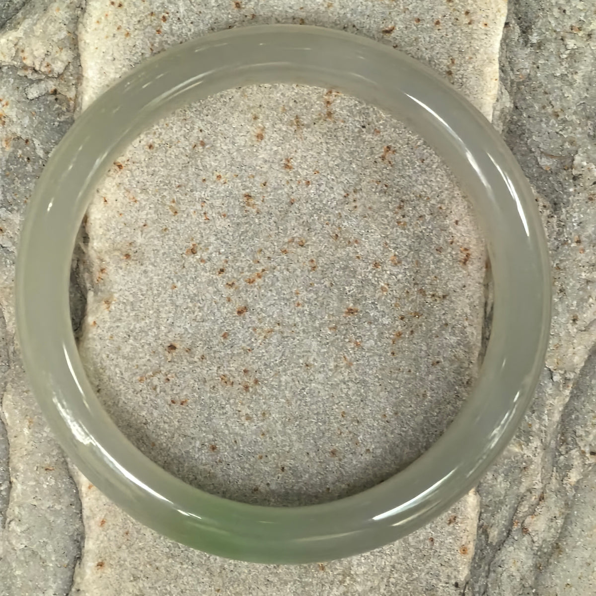 Overhead view of a greenish white Hetian nephrite bangle on stone, showing its circular outline and localized green coloring.