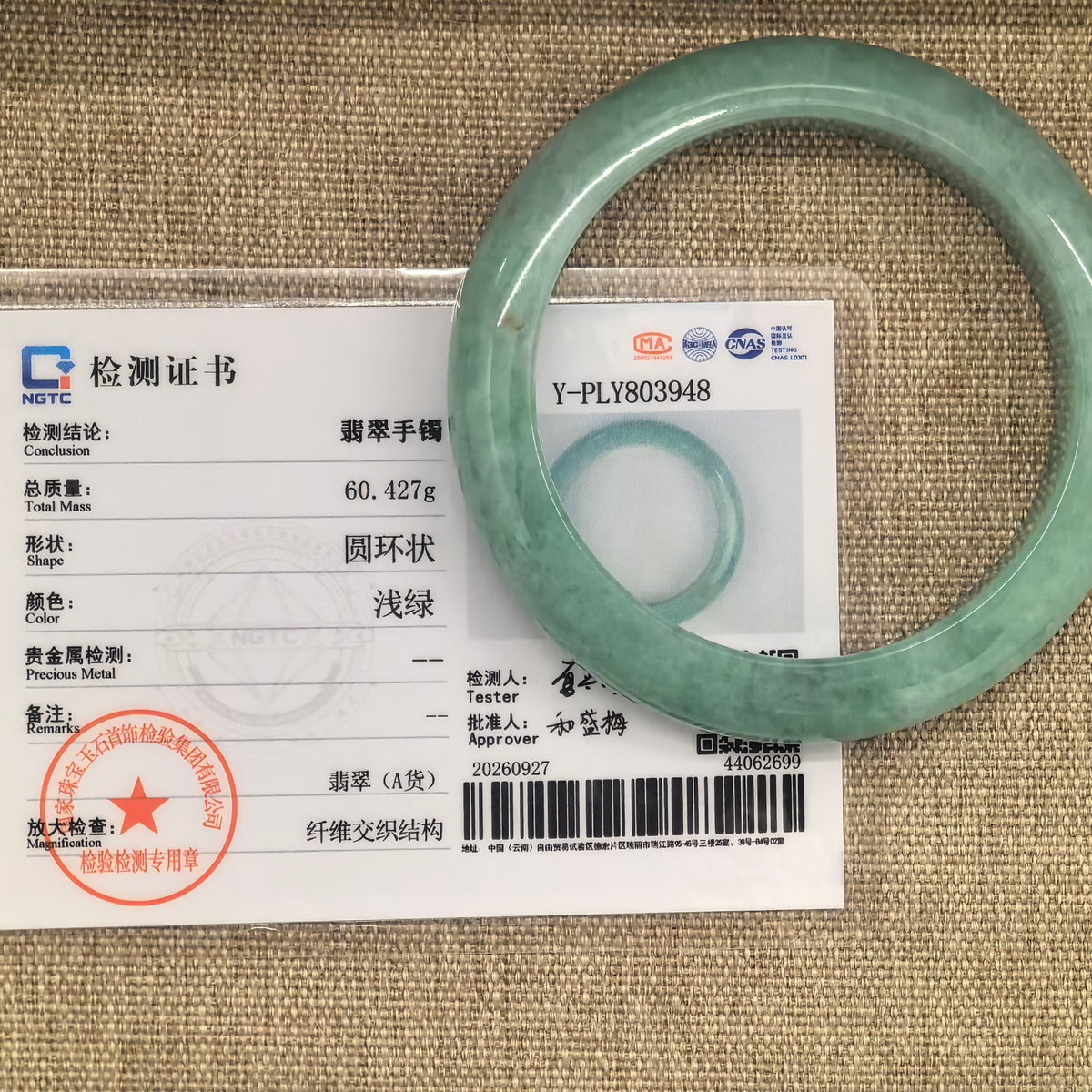Apple green jadeite bangle displayed over its matching NGTC certificate identifying it as Grade-A jadeite.