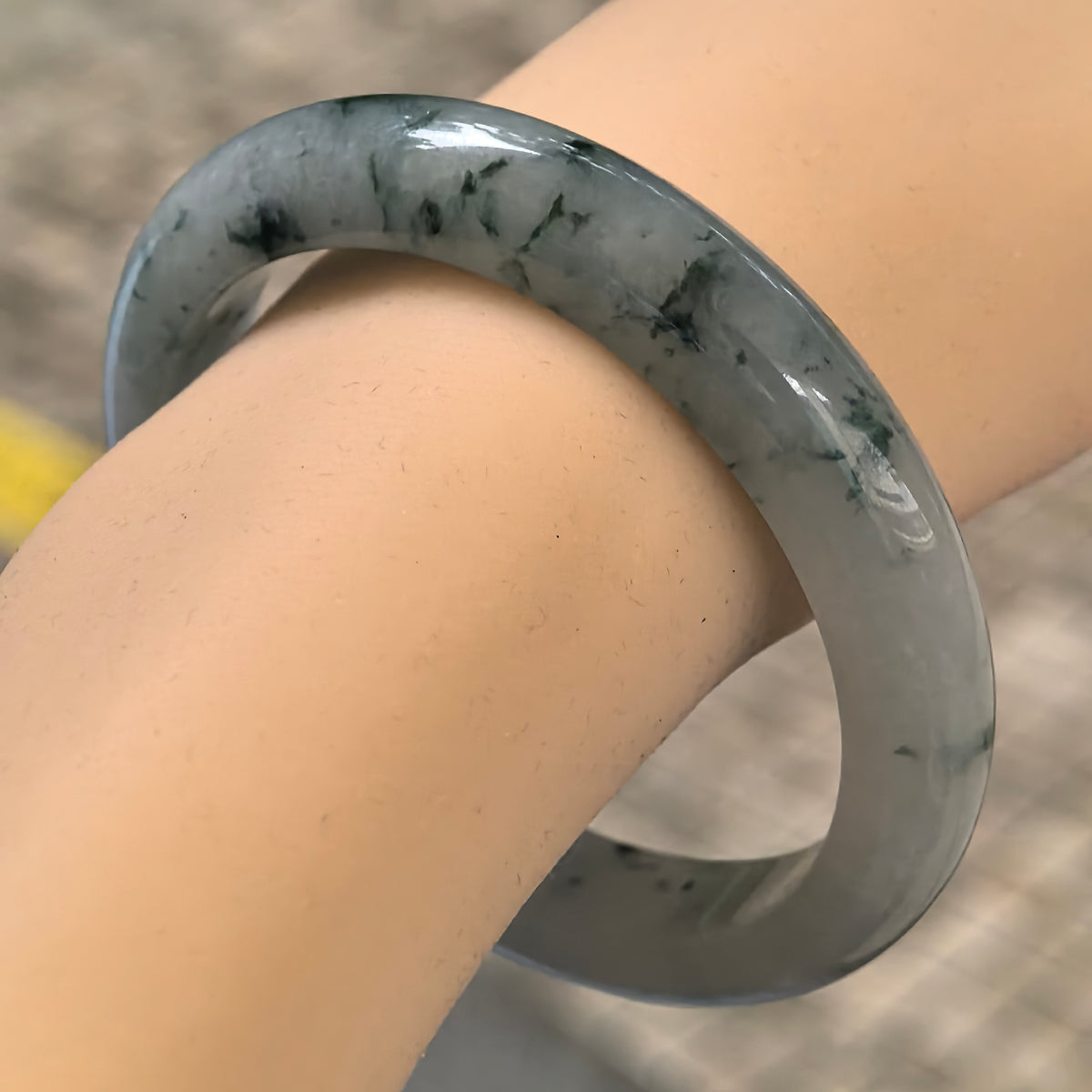 Angled wrist view of an icy glutinous jadeite D-shape bangle with branching deep green floating patterns across a pale green base.
